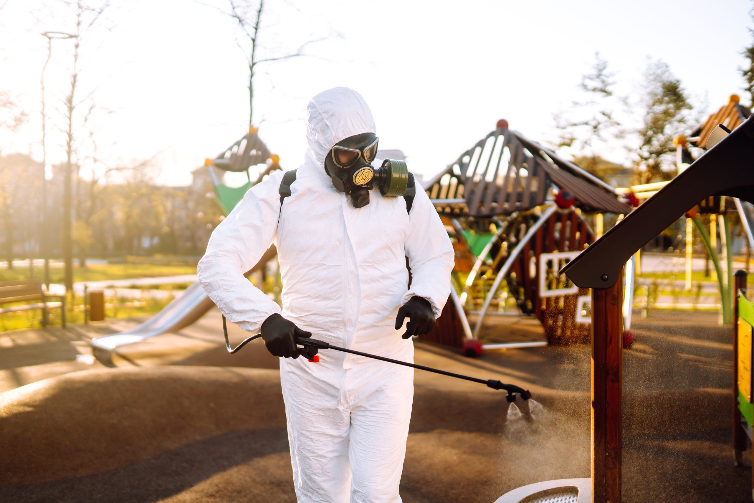 Person in protective hazmat suit disinfecting playground equipment.